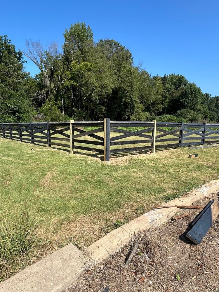 A black ranch style fence along a field
